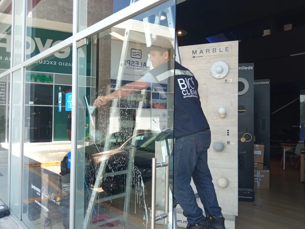 Técnico de BioClean limpiando el cancel de vidrio de un local comercial con jalador y escalera